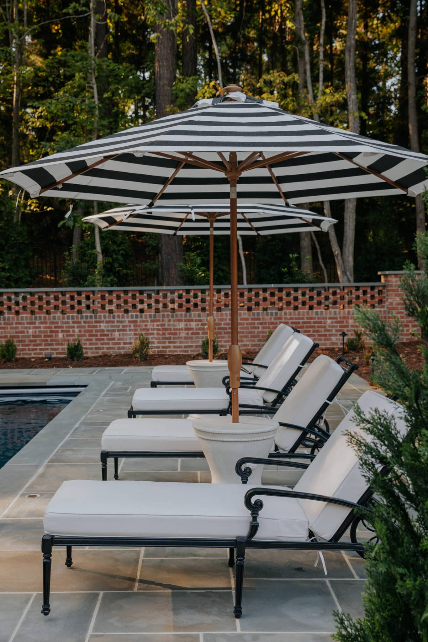 Chris Loves Julia | In-ground pool surrounded by black iron furniture with white cushions under black and white striped umbrellas