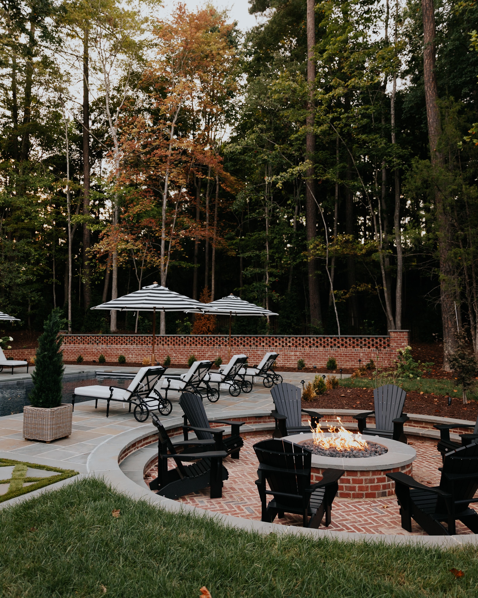 Chris Loves Julia | Outdoor black Adirondack chairs around a fire pit and pool chairs next to a pool