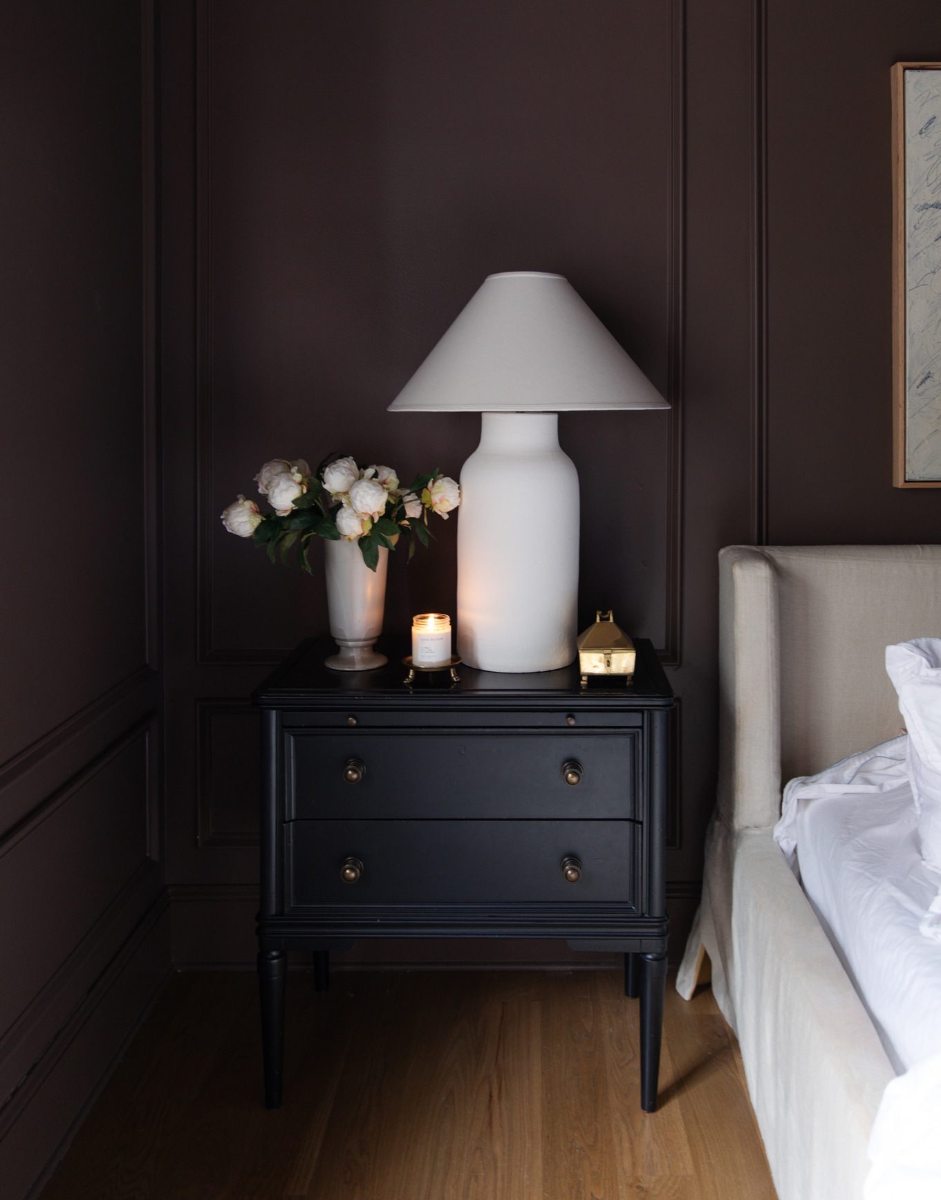 Chris Loves Julia | Candle on a gold footed candlestand on a nightstand in a bedroom