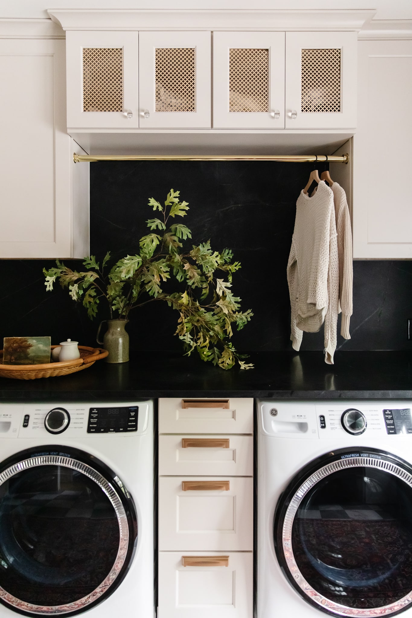 Chris Loves Julia | Laundry room with washer and dryer, cabinets and hanging brass rod 