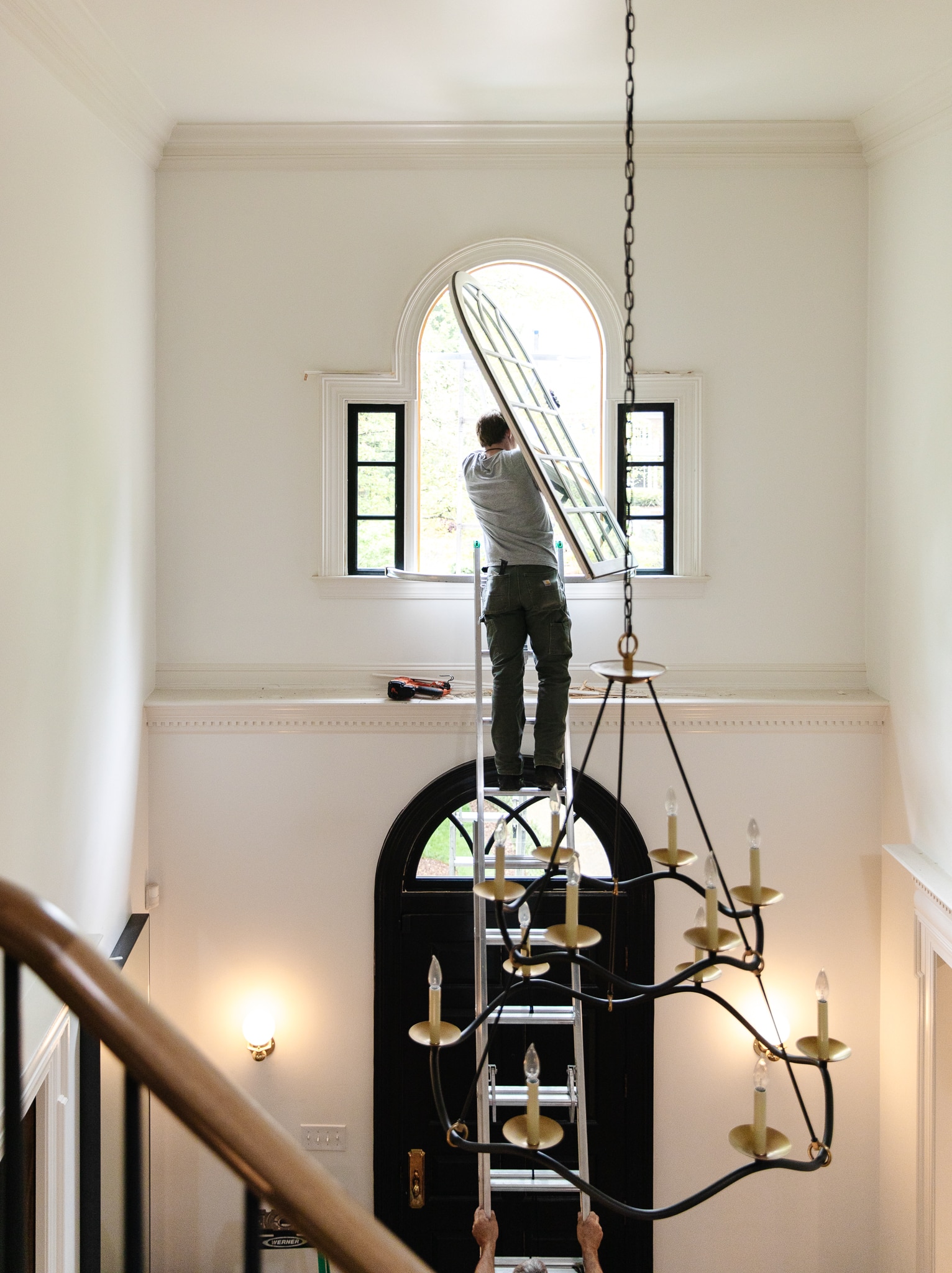 Chris Loves Julia | Man standing on a ladder in an entryway replacing an arched window