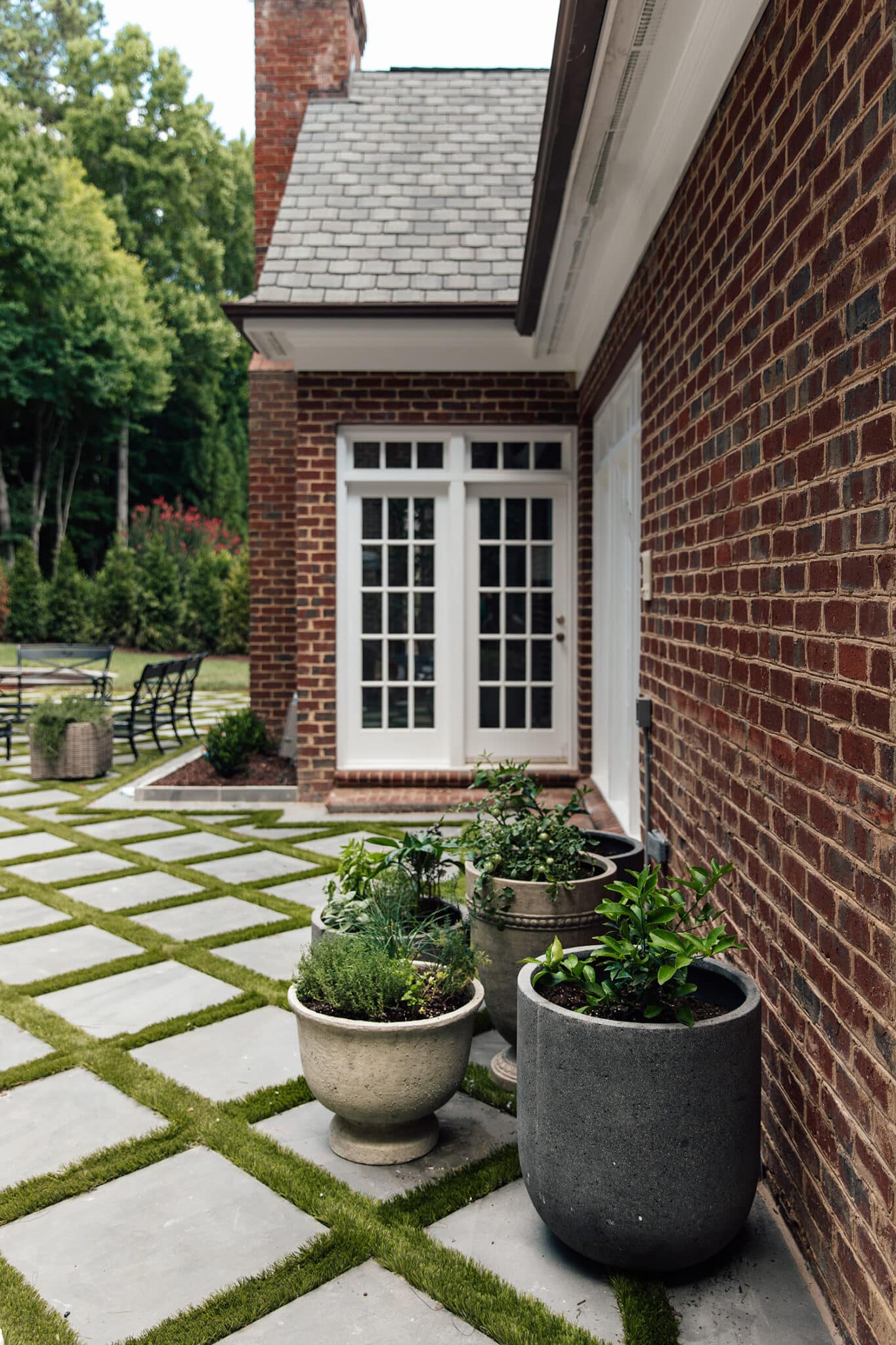 Chris Loves Julia | Stone and concrete outdoor planters with faux boxwood in front of brick house