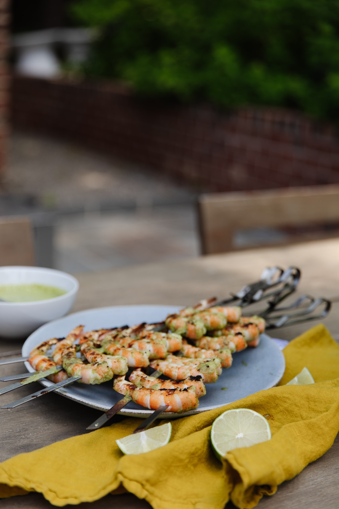 A platter of grilled shrimp skewers next to cut limes on a picnic table